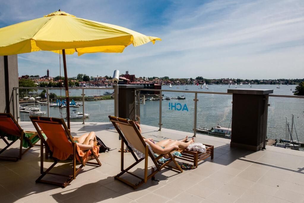 A balcony with lounge chairs, a yellow umbrella, and a view of a marina with boats.