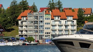 Un edificio de varios pisos con balcones, un cartel que dice 'ACHI' y un puerto deportivo con barcos.