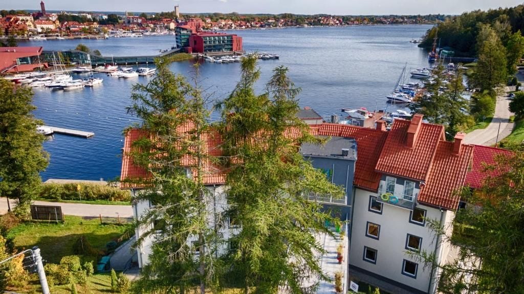 A marina with boats, a building with red roofs, and a view of a town across the water.