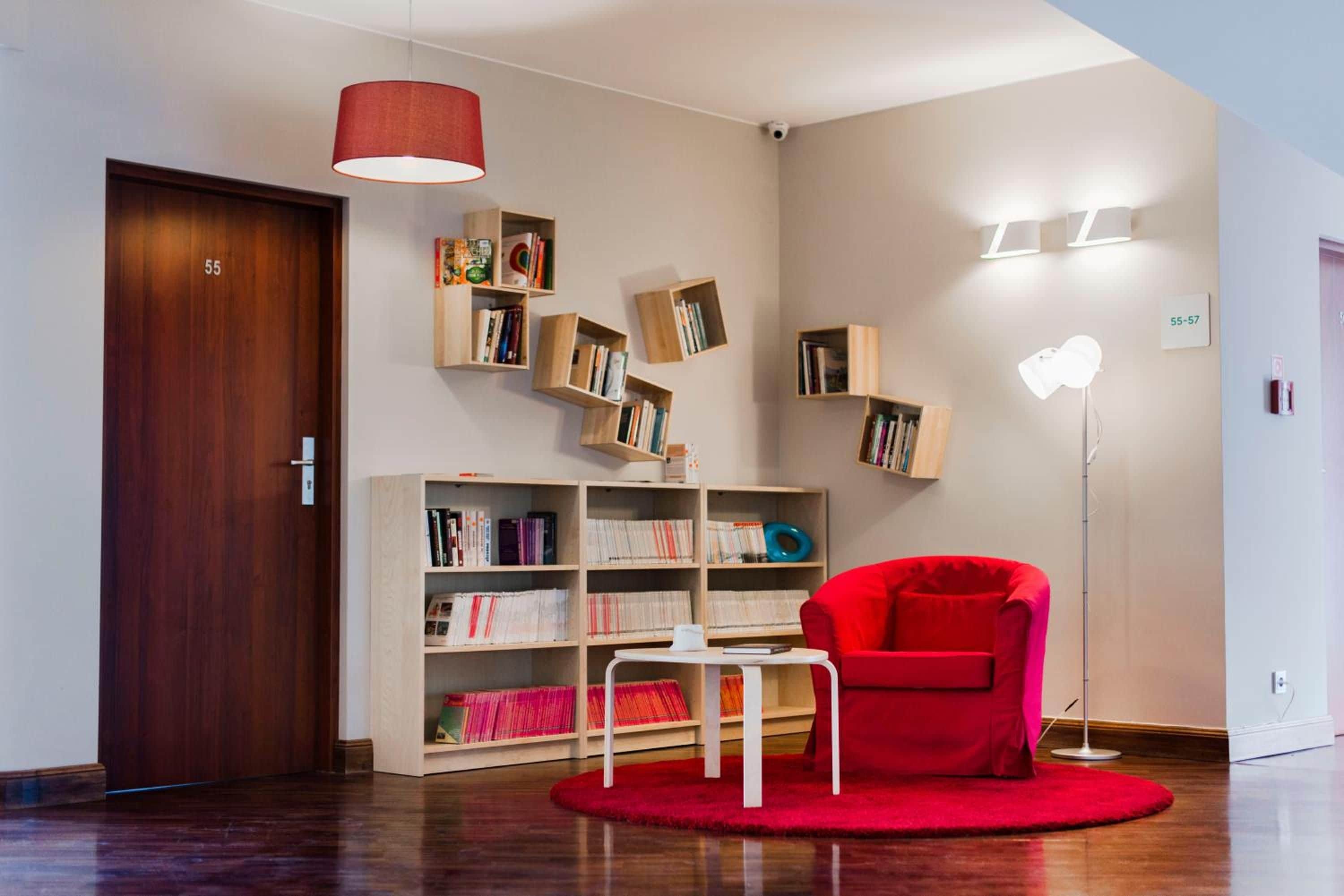 Una habitación con puerta de madera, una silla roja, una estantería y una lámpara de pie.