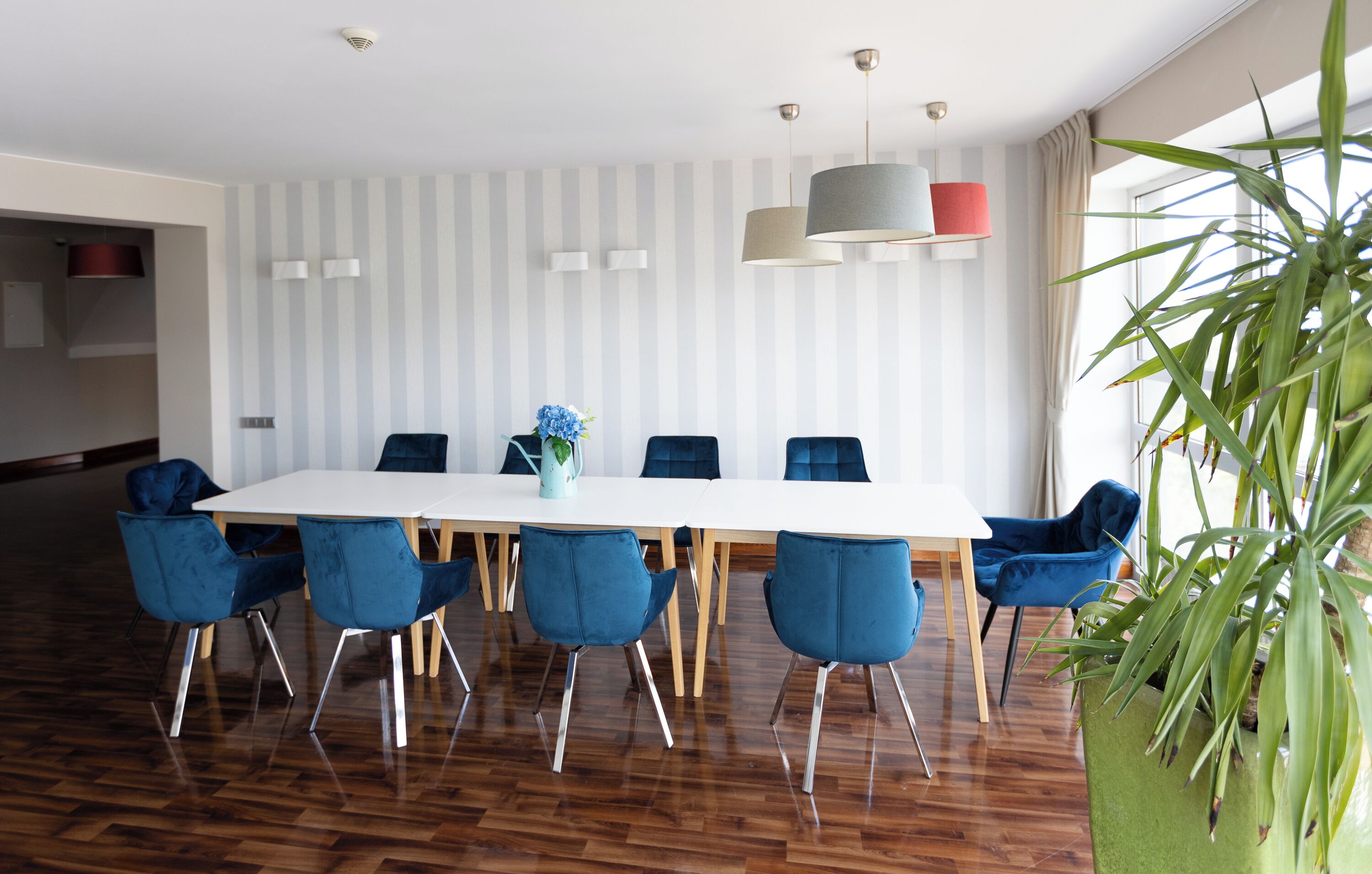 Un espace repas moderne avec une table blanche, des chaises bleues et une grande plante en pot.