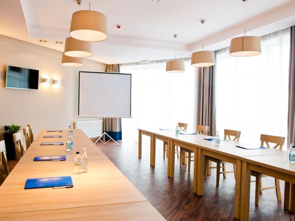 A conference room with a long table, chairs, a projector screen, and pendant lighting.