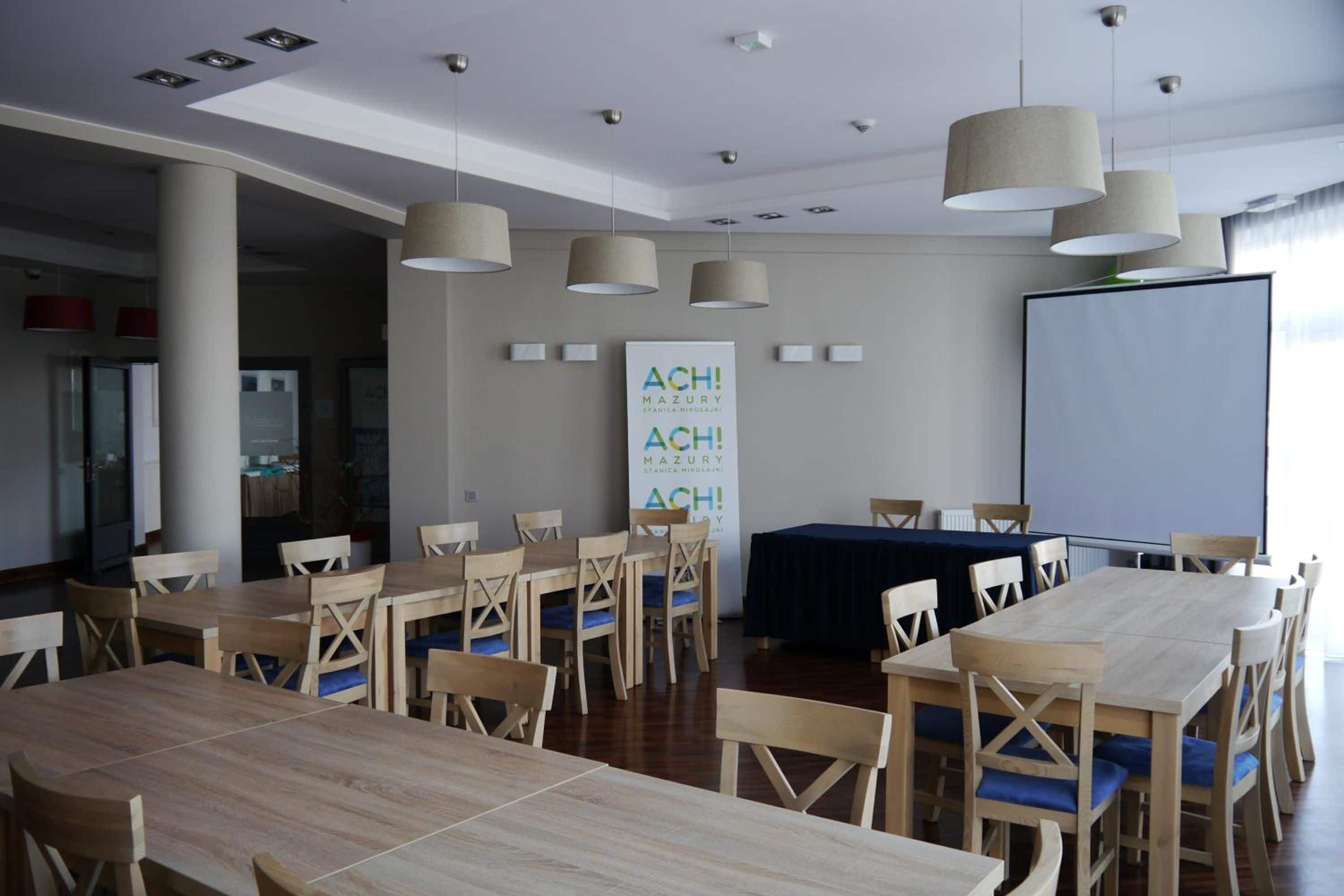 A conference room with multiple tables and chairs, a projector screen, and a banner on the wall.