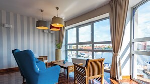 Una habitación moderna con un ventanal grande, muebles de madera y vistas a barcos.