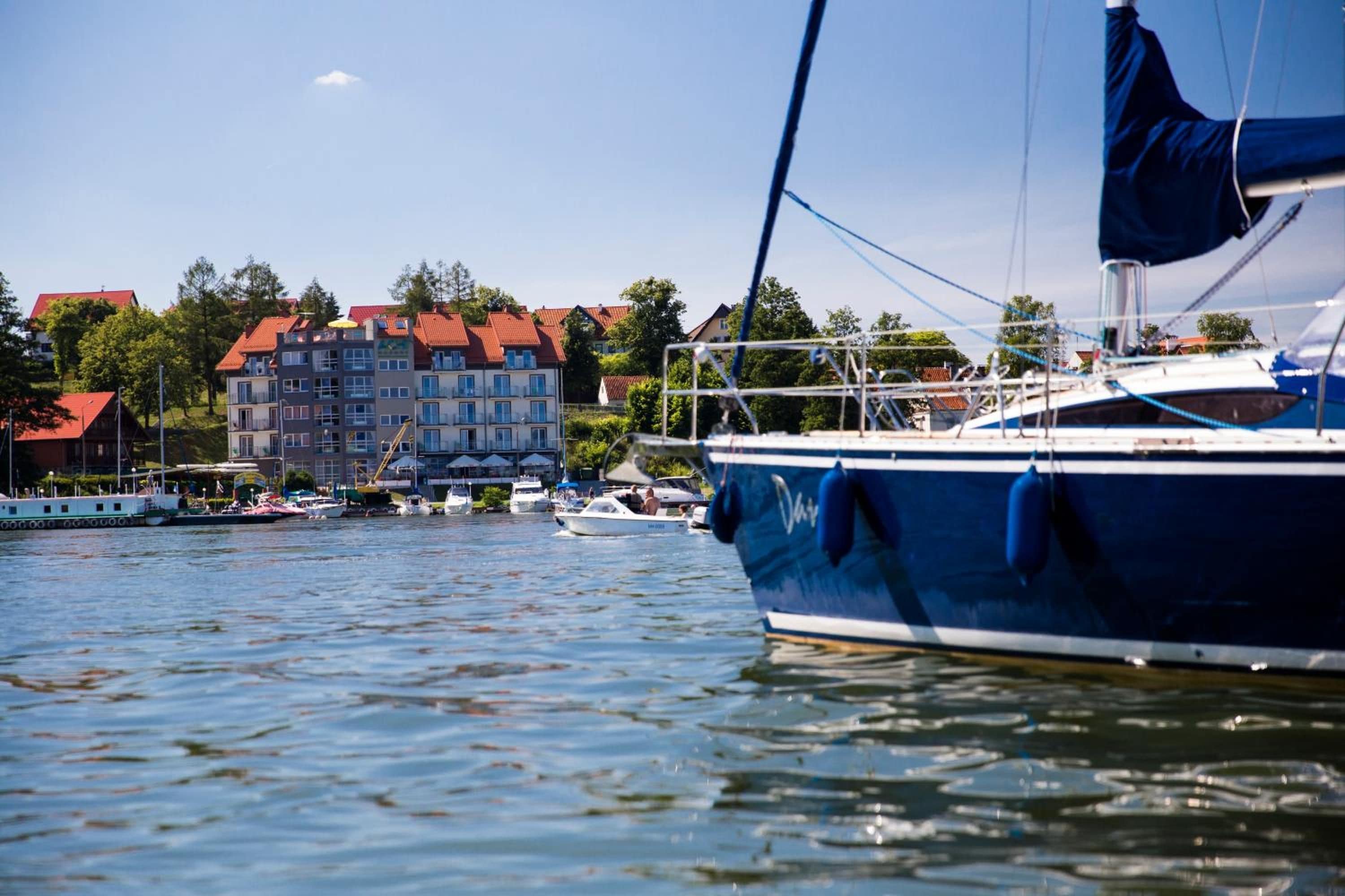 Ein Yachthafen mit vertäuten Booten, ein großes Gebäude mit roten Dächern im Hintergrund und ein klarer Himmel.