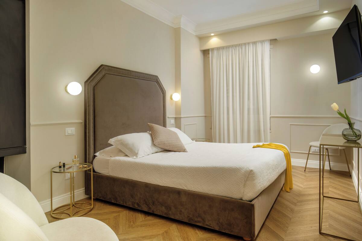 A bedroom with a large bed, bedside tables, a flat-screen TV, and a window with curtains.
