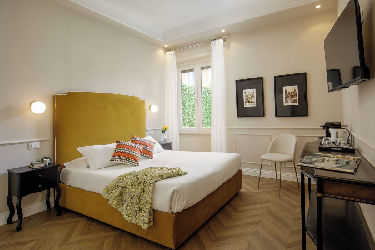A neatly arranged bedroom with a bed, bedside table, chair, and a desk with a flat-screen TV.