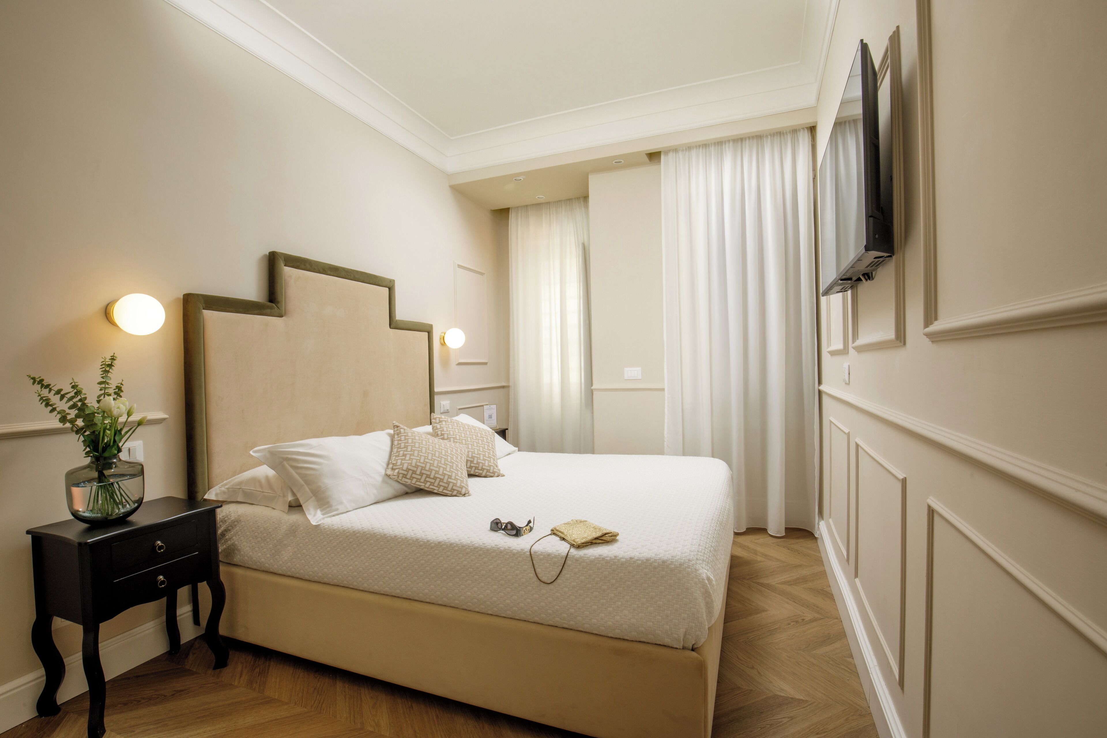 Un dormitorio ordenado con cama, mesita de noche y televisor montado en la pared.