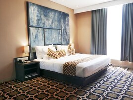 Una habitación de hotel con una cama grande, una mesita de noche con lámpara y una alfombra estampada.