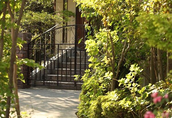 A gated entrance with a metal gate, surrounded by lush greenery and a stone wall. - Ryokan Pinon (Shibukawa)