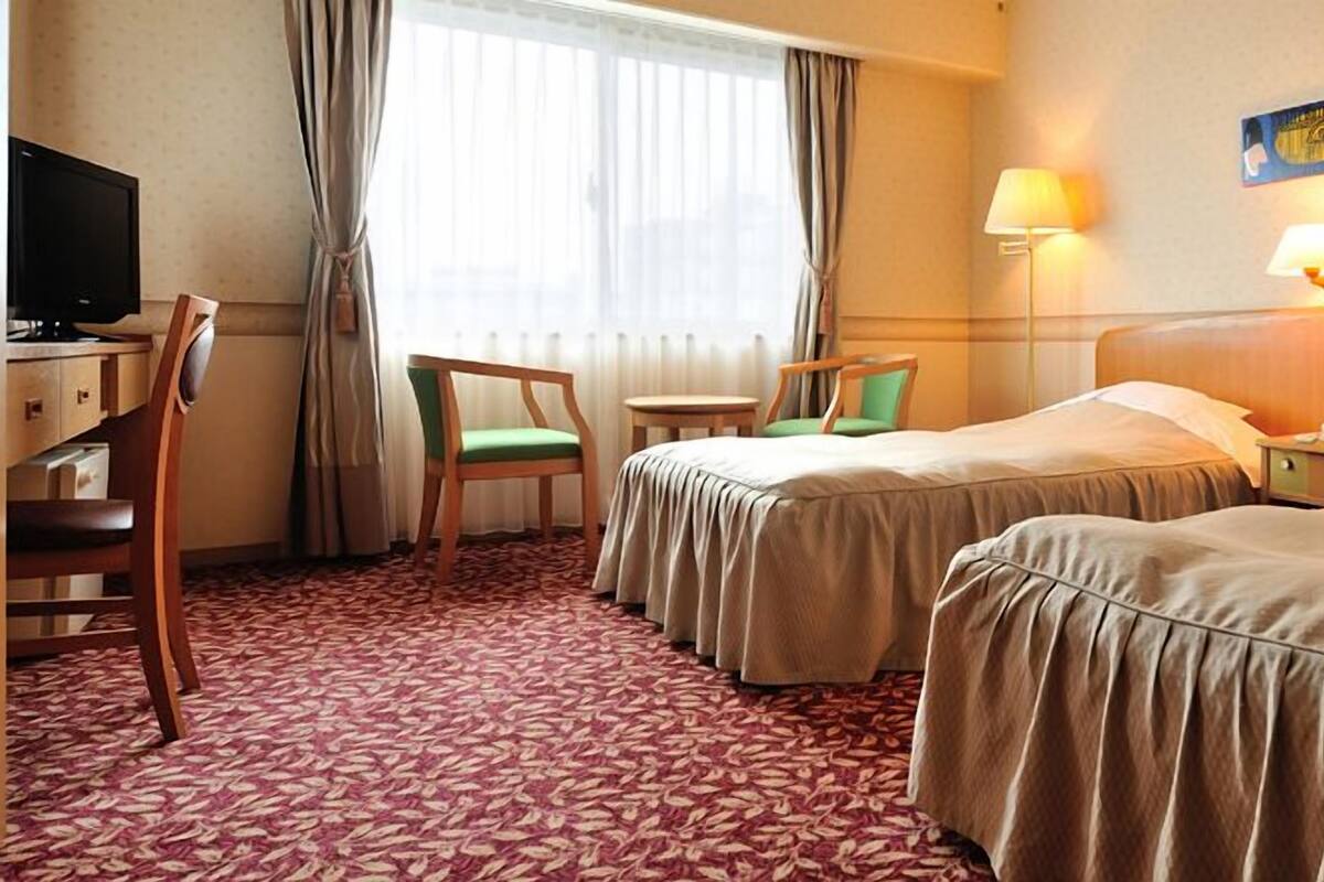 Habitación de hotel con dos camas, un escritorio con televisor, una mesita y sillas.