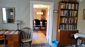A cozy living room with a dining area, a bookshelf filled with books, and a mirror on the wall. - Brunnsta Gård (Balsta)