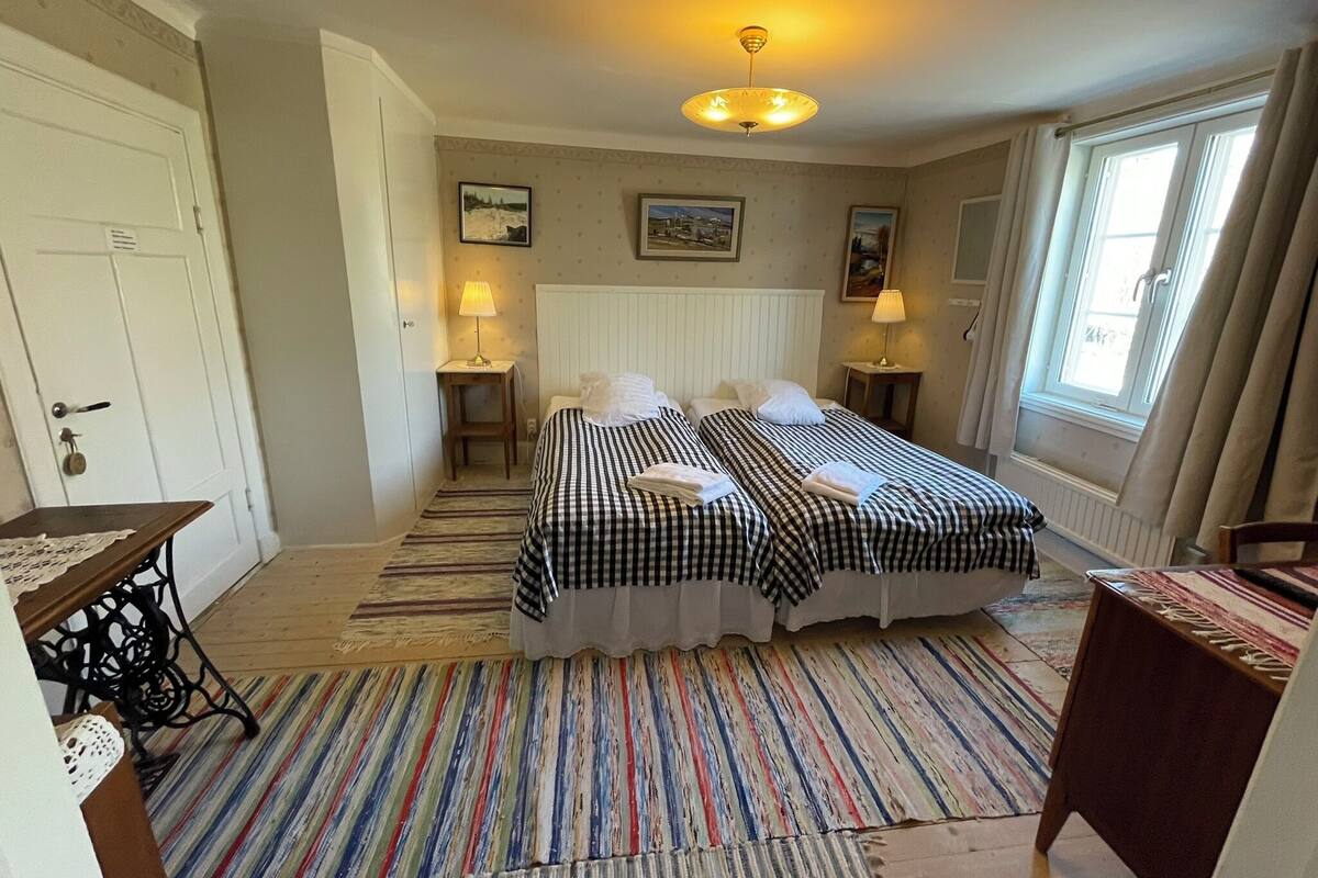 A bedroom with two beds, a table, a chair, a radiator, and a window.