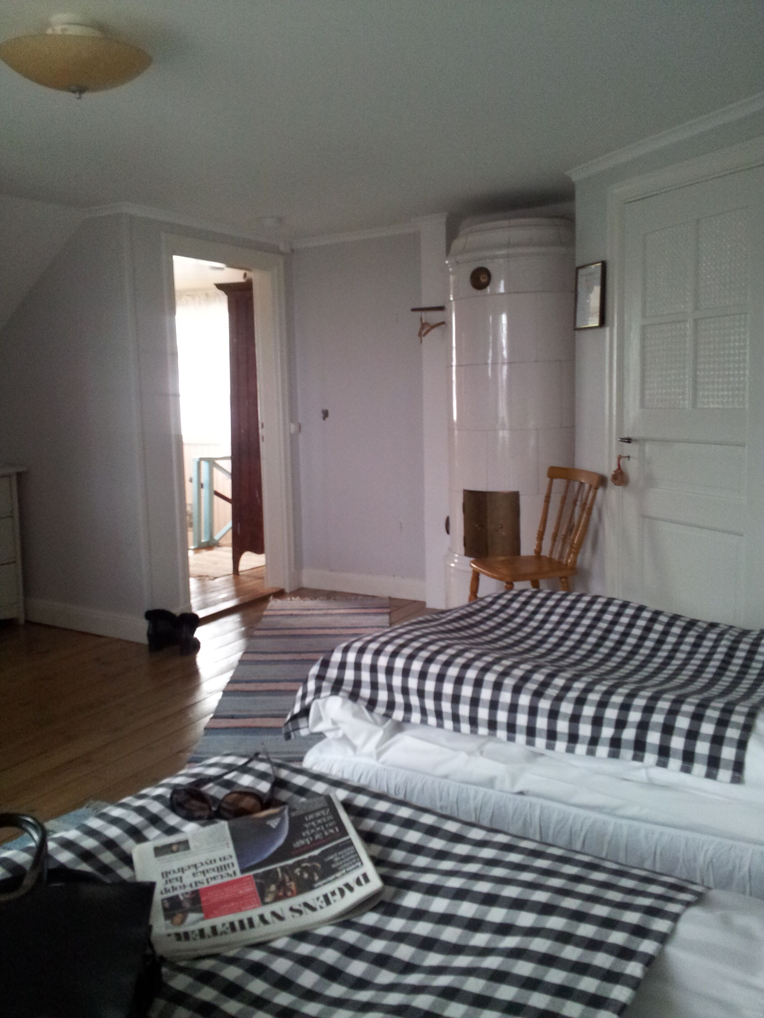 A bedroom with two beds, a wooden floor, a door leading outside, and a small table with a newspaper.