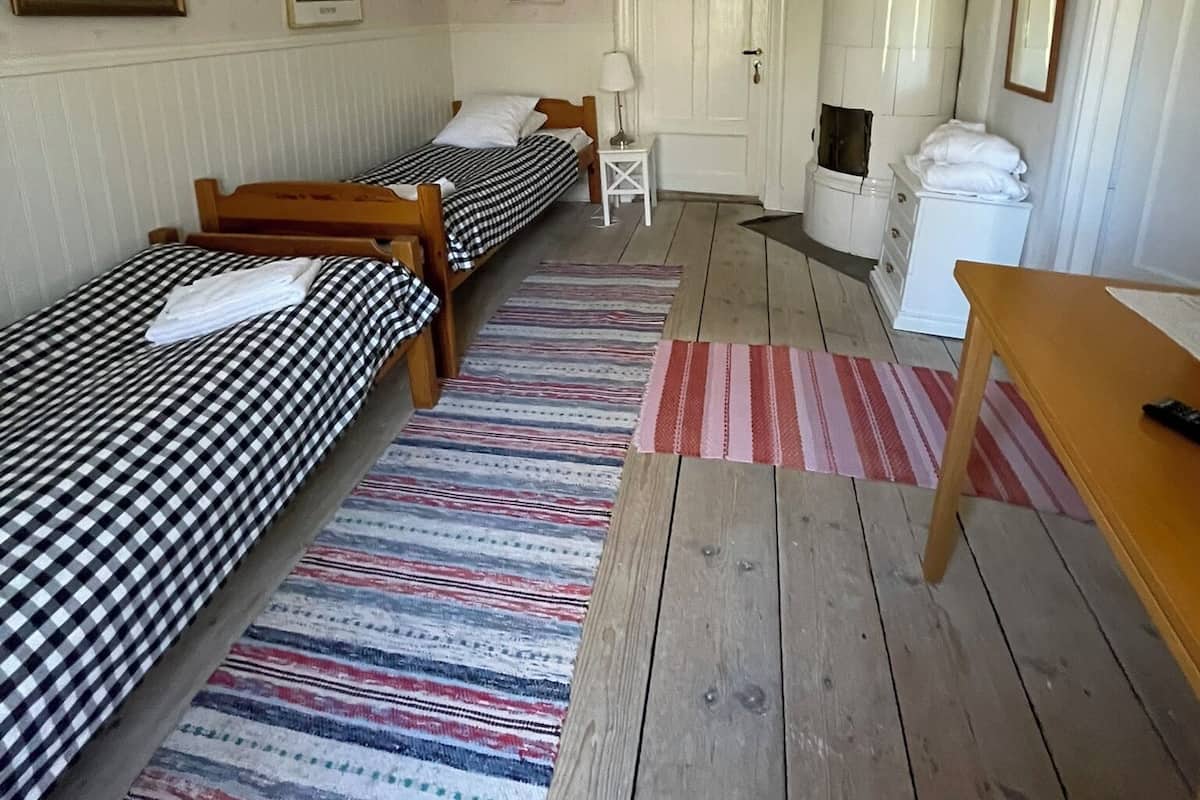 A room with two single beds, a wooden table, a white cabinet, and a door leading to another room.