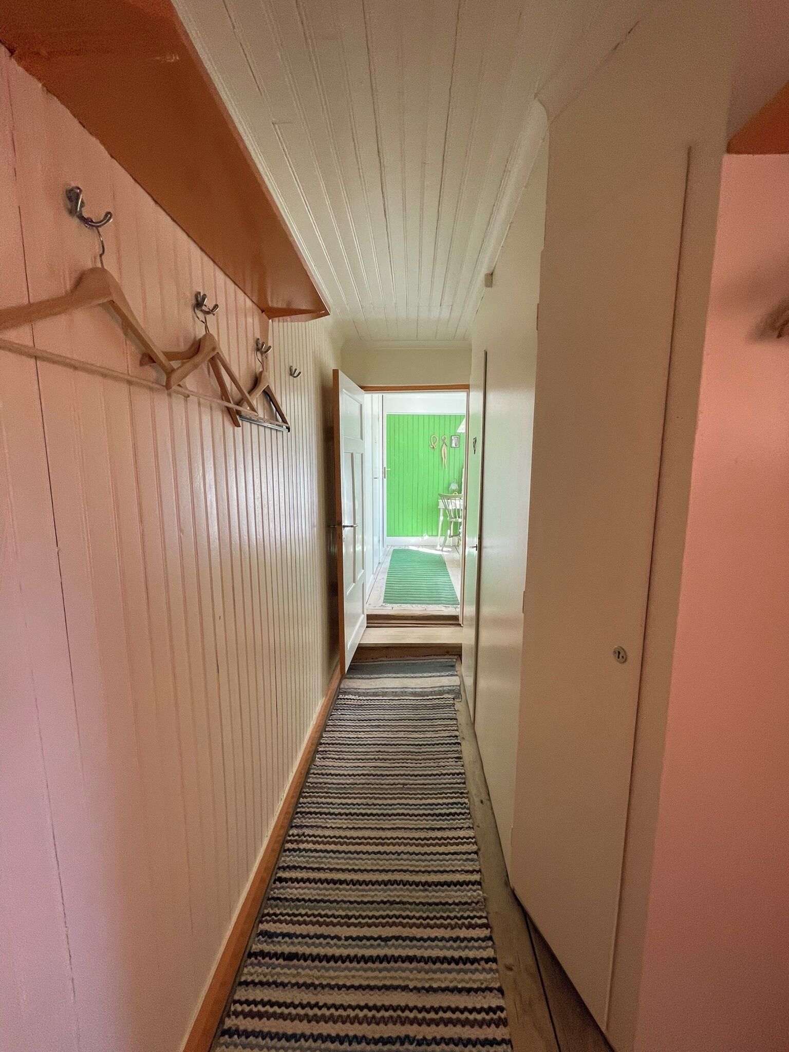 A narrow hallway with wooden paneling, a striped rug, and a green door at the end.
