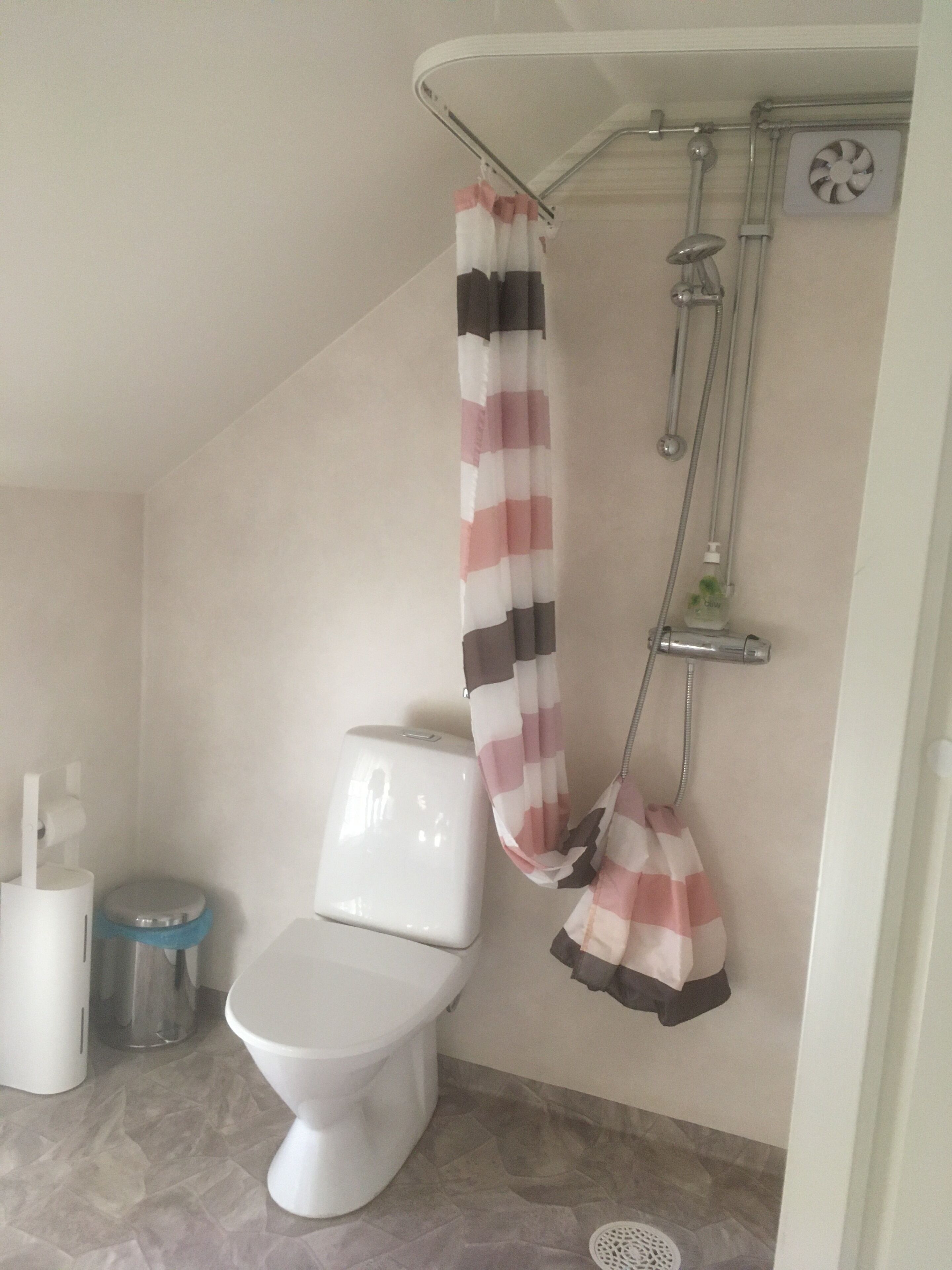A bathroom with a toilet, a shower with a striped shower curtain, and a hand dryer.