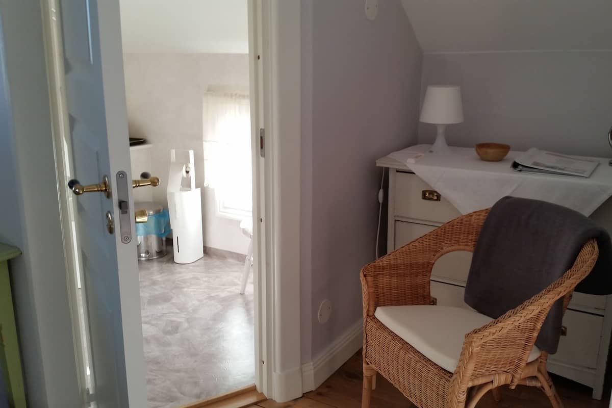 A room with a wicker chair, a small table with a lamp, and a white desk with drawers.
