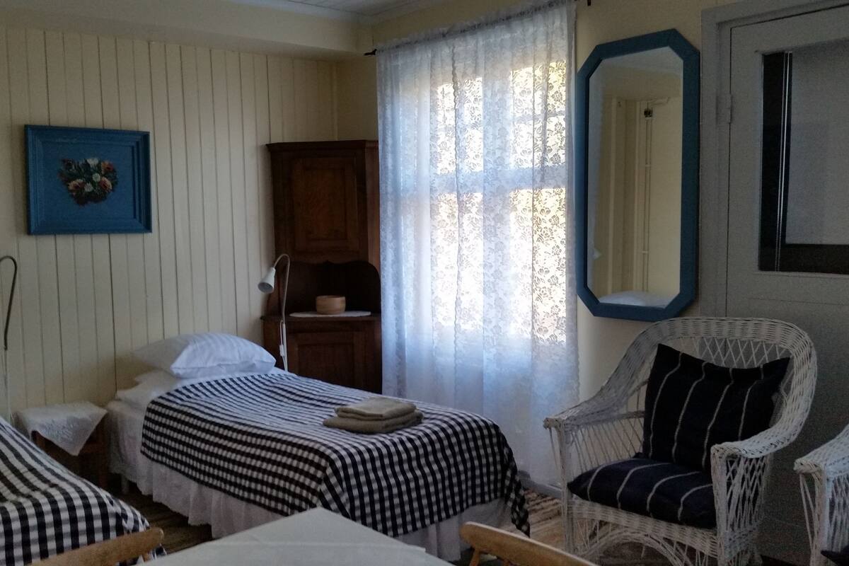 A room with two beds, a wooden cabinet, a mirror, and wicker chairs.