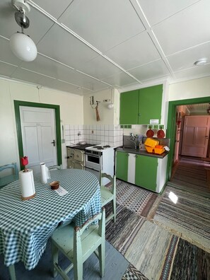 A kitchen with a stove, sink, and green cabinets. There is a table with a checkered tablecloth and chairs. - Brunnsta Gård (Balsta)