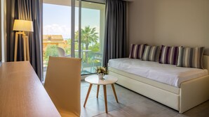 A modern hotel room with a sofa, a small round table with a lamp, and a view of palm trees through the glass door. - CNic Gemini Hotel (Corfu)