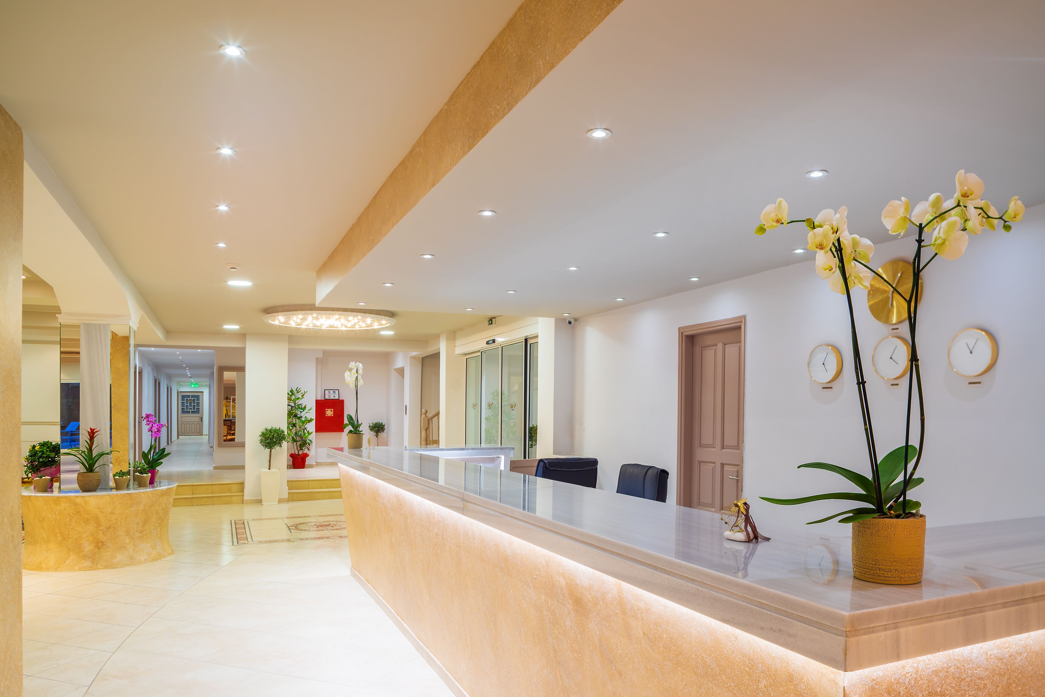 Ein Hotel-Empfangsbereich mit einer Marmor-Theke, Zimmerpflanzen und einem modernen Kronleuchter.