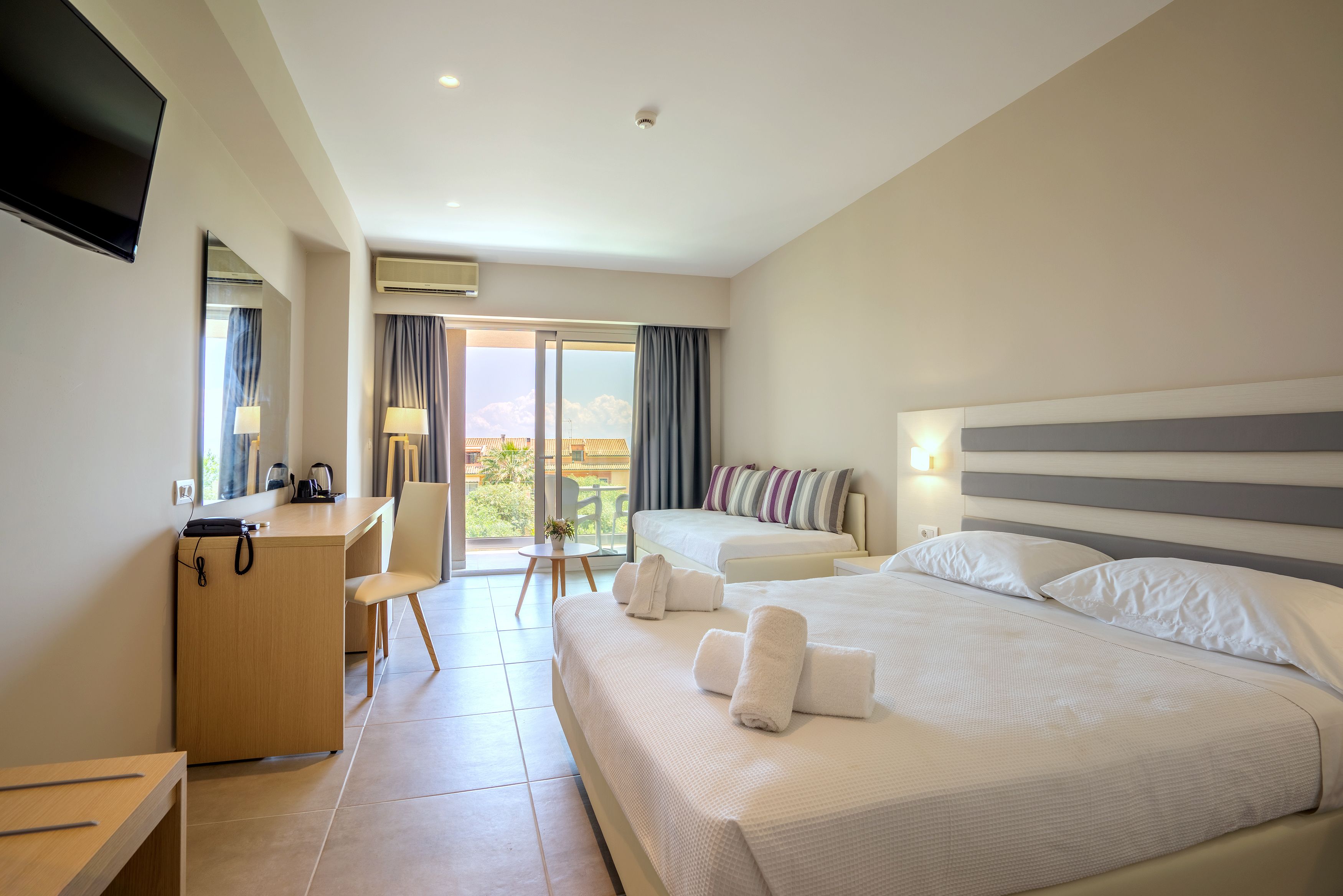 Ein Hotelzimmer mit Bett, Schreibtisch, Stuhl, Fernseher und einem Balkon mit Blick.