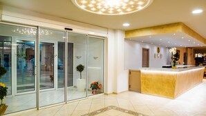 A modern hotel lobby with a reception desk, glass doors, and a ceiling light fixture. - CNic Gemini Hotel (Corfu)