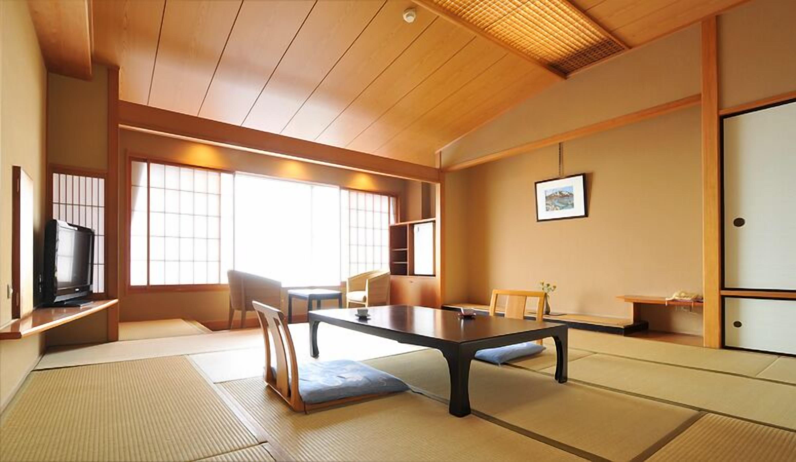A traditional Japanese-style room with tatami flooring, a low table, and a television on a shelf.