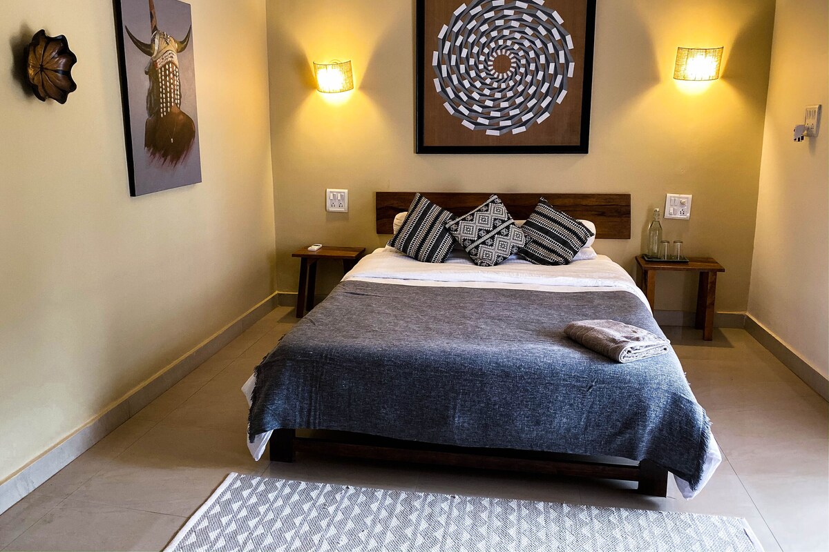 Quarto bem arrumado com uma cama grande, duas mesas de cabeceira, uma obra de arte na parede e duas arandelas.