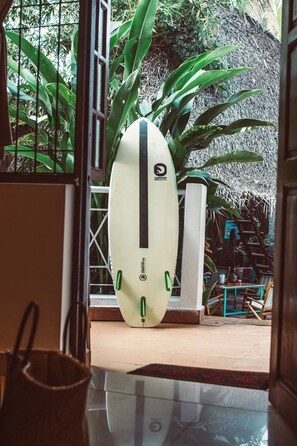 Uma prancha de surf encostada na parede de um quarto com uma mesa de vidro e cadeiras.