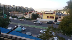 A street view with multiple cars parked along the roadside, buildings in the background, and a clear sky. - Marom Ziv Center - Newe Shaanan (Haifa)