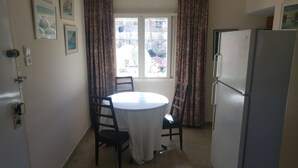 A small kitchen with a round table, chairs, a refrigerator, and patterned curtains. - Marom Ziv Center - Newe Shaanan (Haifa)