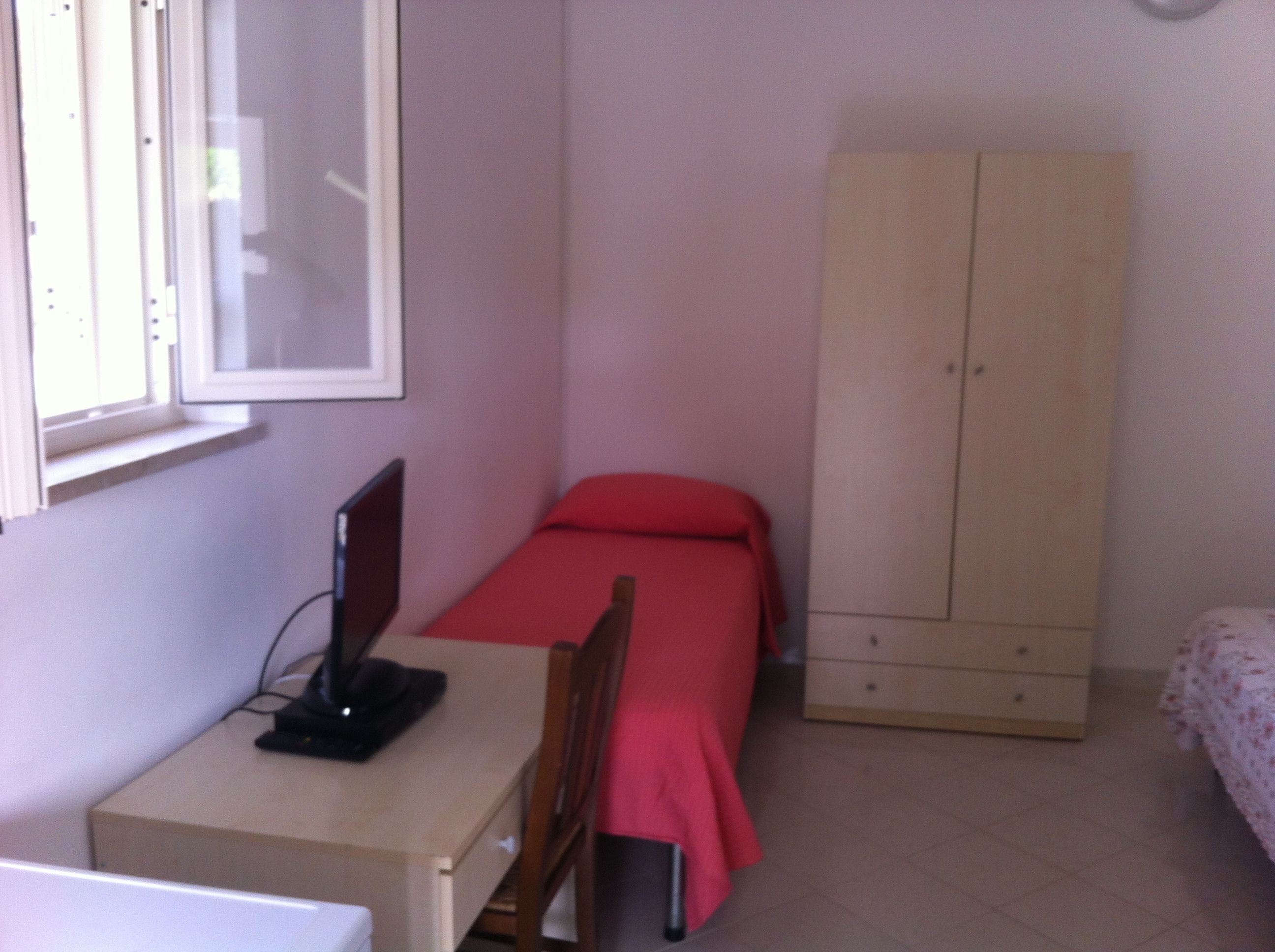 Une petite pièce comprenant un lit simple, un bureau avec un ordinateur et une armoire.