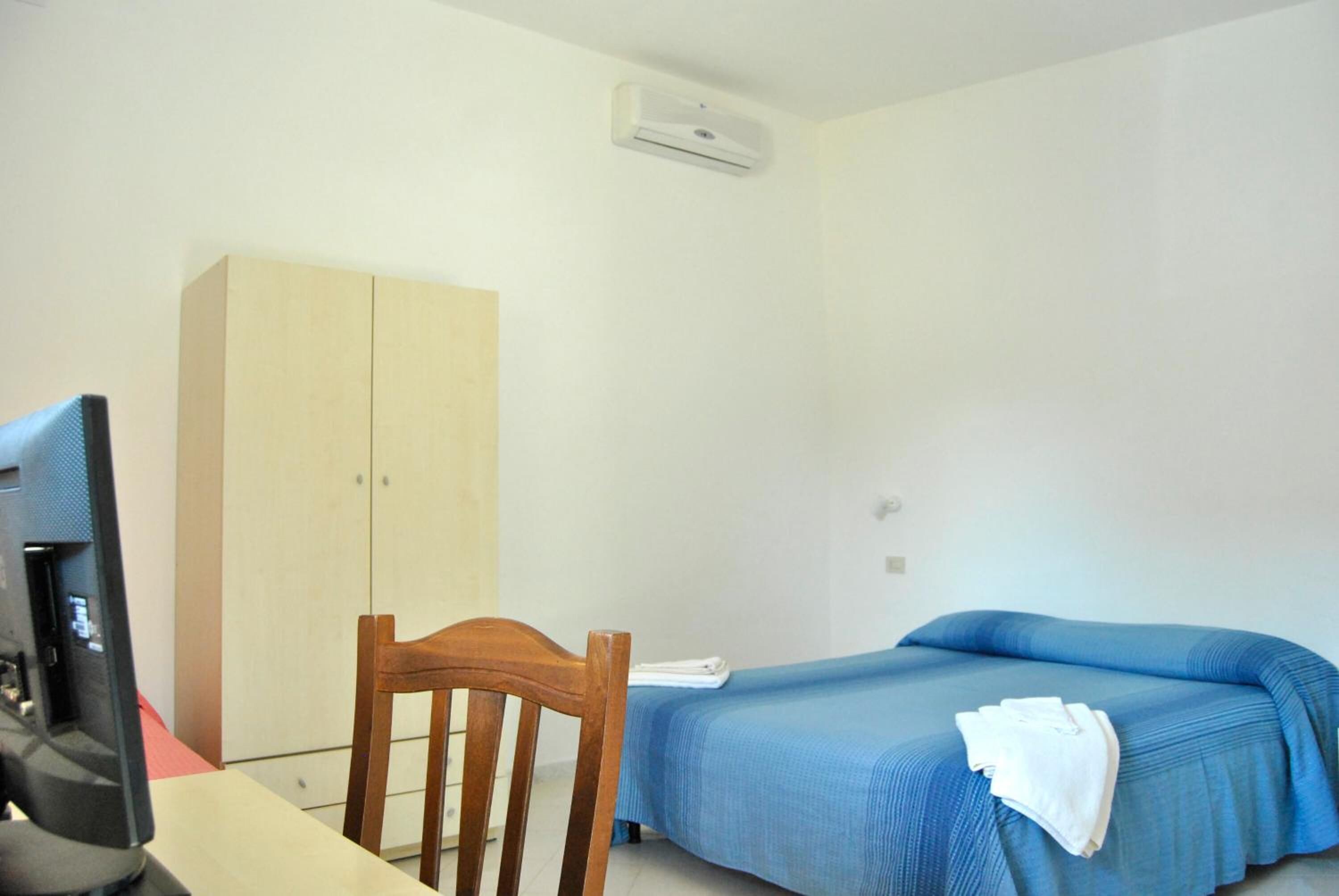 A simple room with a bed, a desk with a computer, a wardrobe, and a wall-mounted air conditioner.