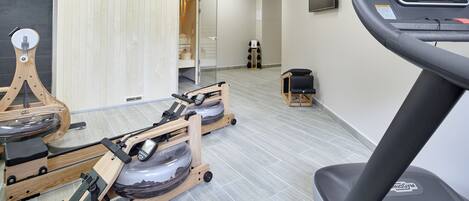 Ein Fitnessstudio mit Laufbändern, Rudergeräten und einer Spiegelwand.