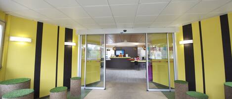 An office interior with a reception desk, glass partitions, and a ceiling with a grid pattern.
