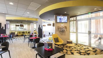 A modern indoor space with a curved yellow wall, a large window, and a seating area with tables and chairs.