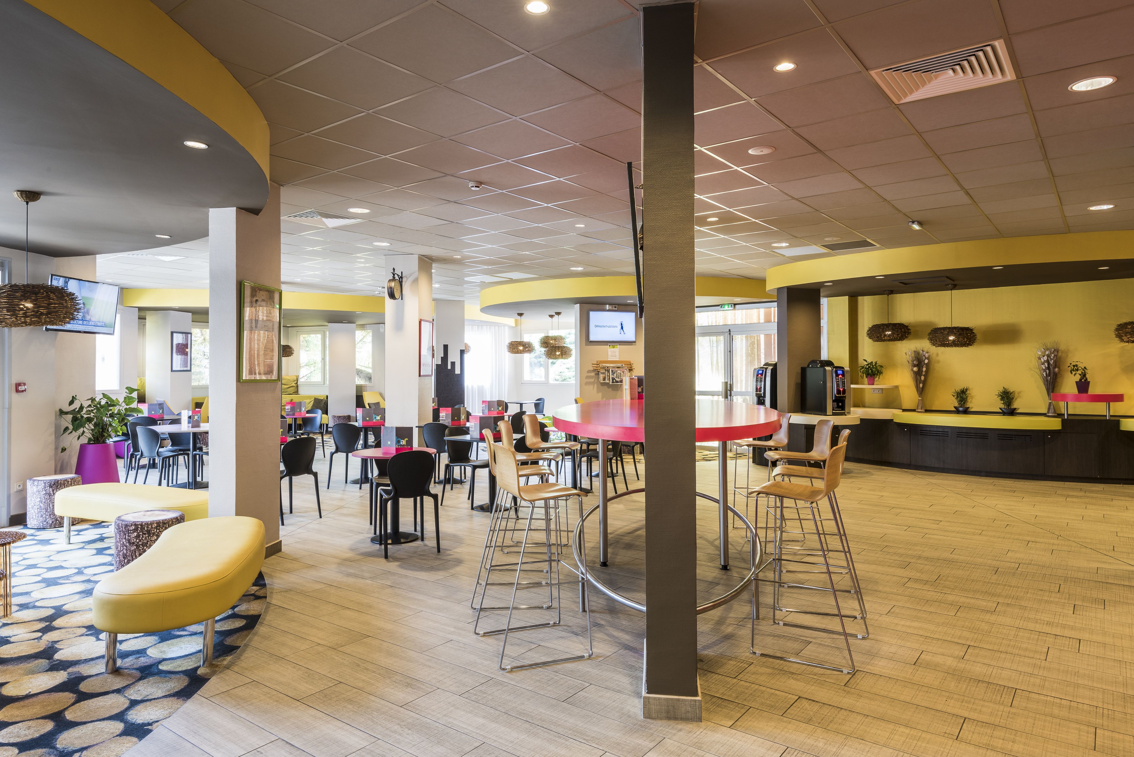 A spacious lobby with multiple seating areas, a reception desk, and a large TV screen.