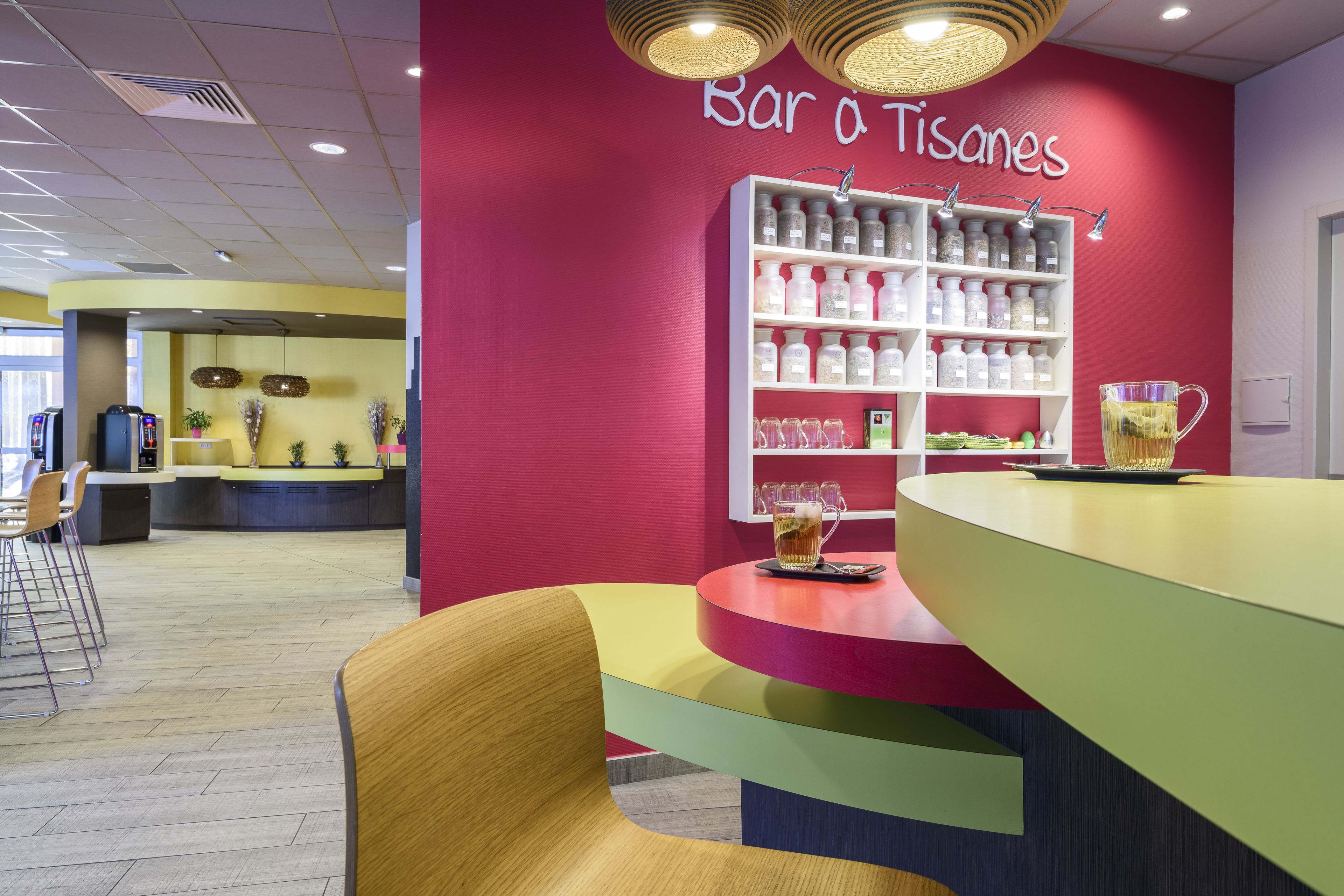 Un espace bar avec un mur rouge, une étagère remplie de bouteilles et un comptoir avec des tabourets.