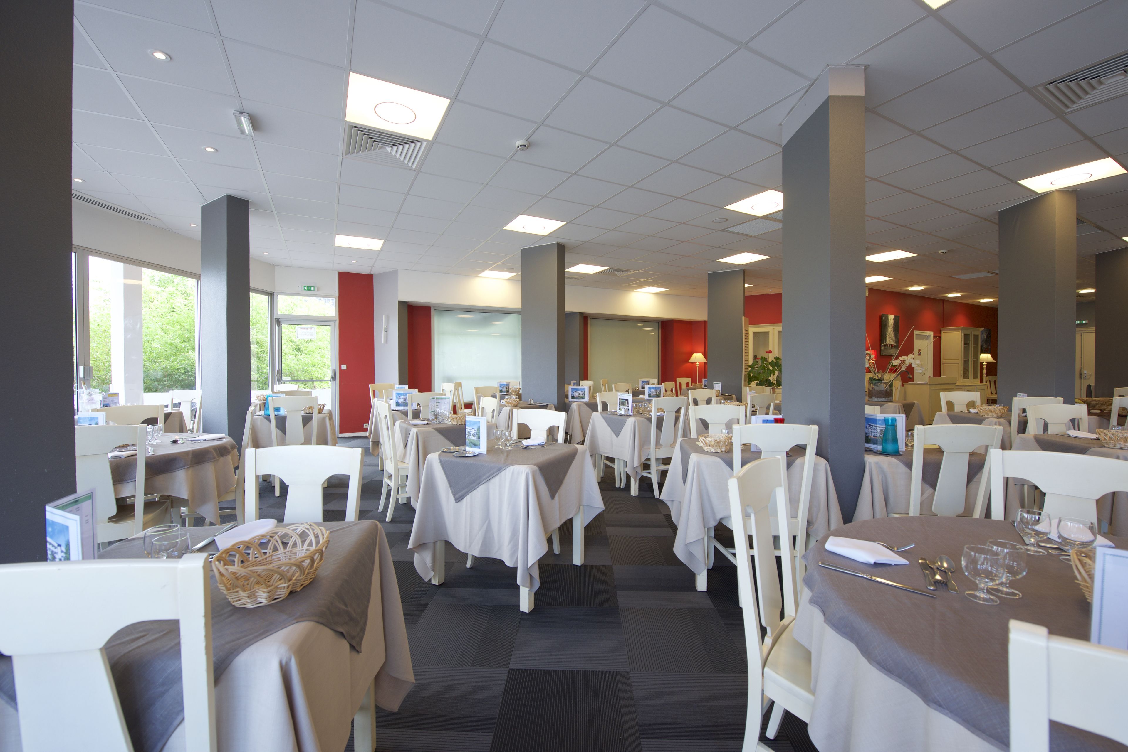 Un comedor espacioso con múltiples mesas y sillas, ventanas amplias y un diseño de techo moderno.
