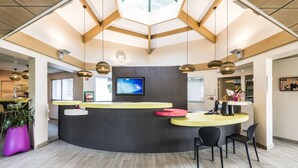 A reception area with a curved counter, a flat-screen TV, and a modern ceiling design. - Hôtel Miradour (Dax)