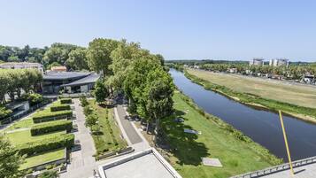 A riverside walkway with a modern building, green lawns, and a clear sky.
