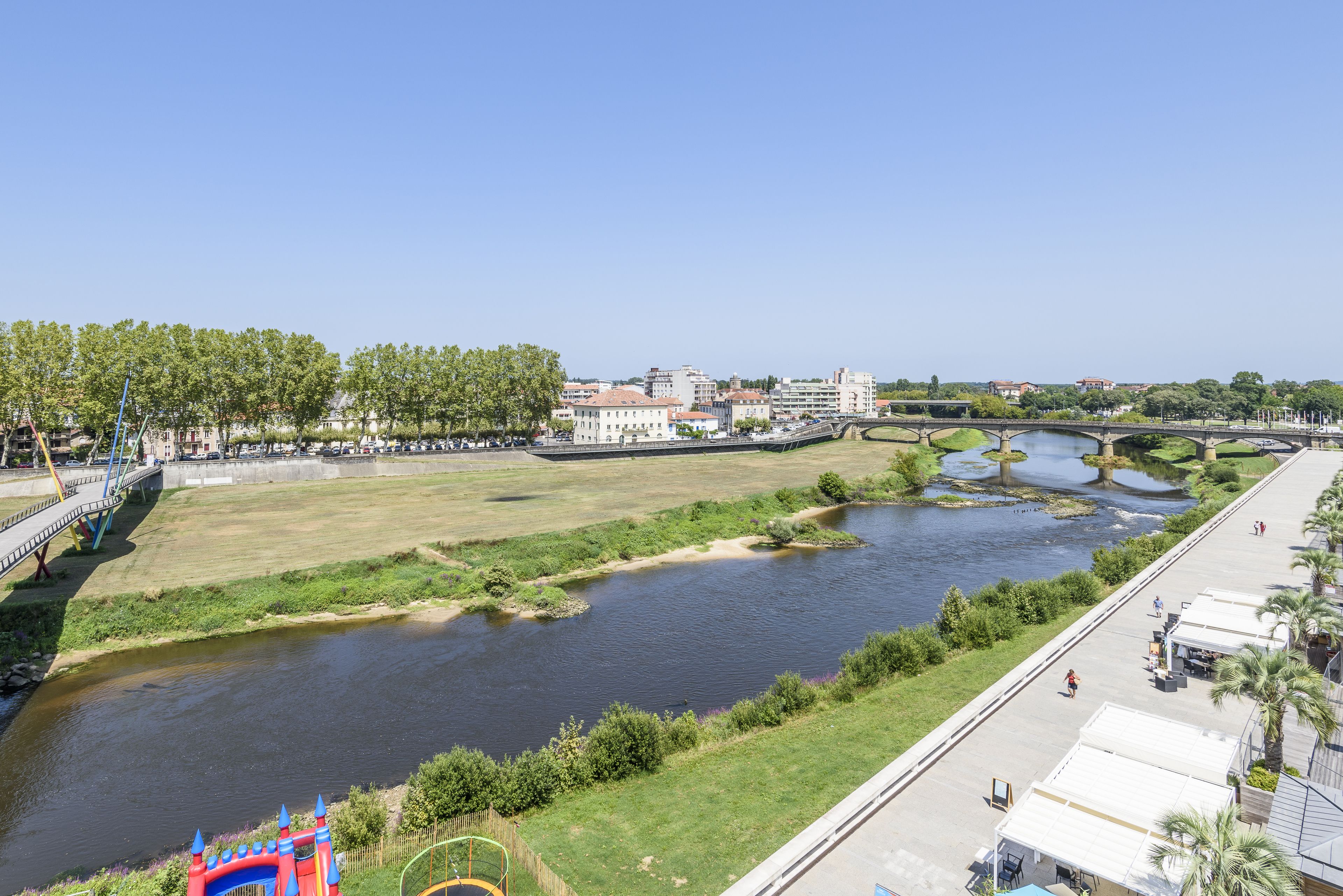 Aussicht auf einen Fluss mit einer Brücke, Grünflächen und Gebäuden im Hintergrund.