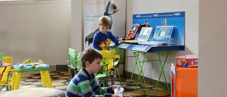 A child playing with a toy in a room with a table, chairs, and a poster on the wall.