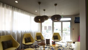 A hotel lobby with yellow chairs, a patterned floor, and a television on the wall. - Hôtel Miradour (Dax)