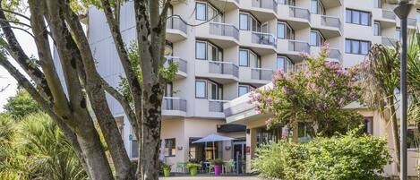 A multi-story hotel with balconies, outdoor seating, and lush greenery.