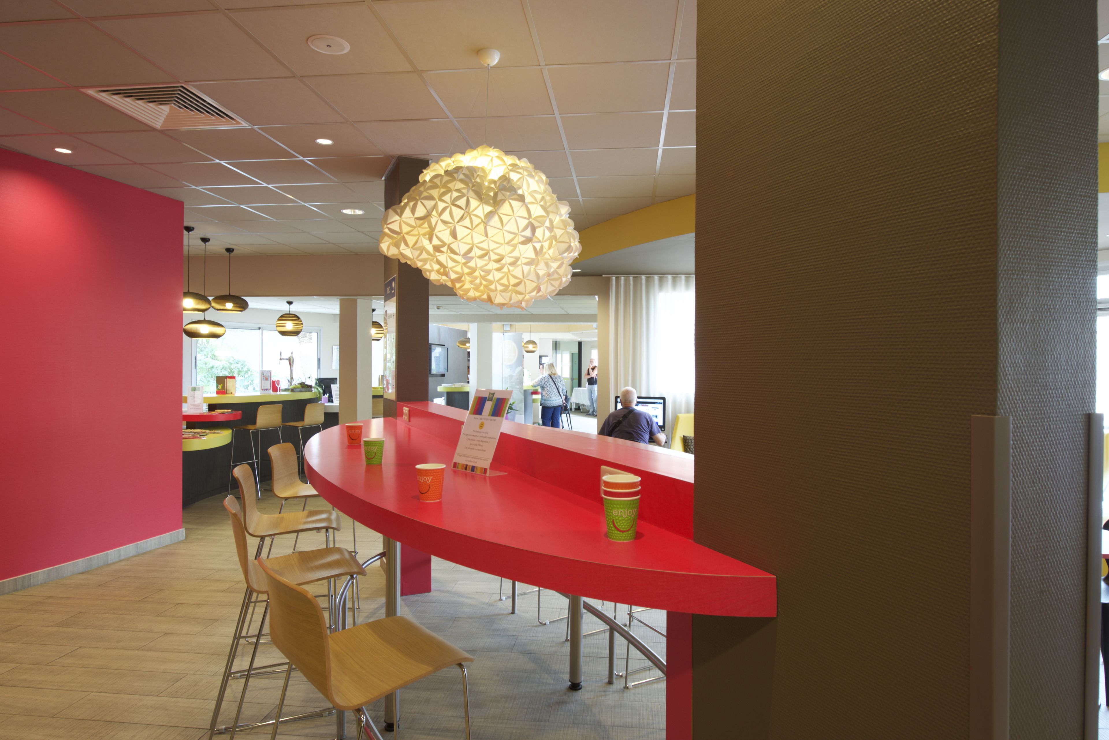 Un interior moderno con una barra roja curva, sillas de madera e iluminación colgante.