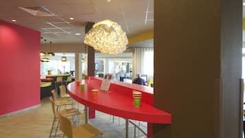 Un interior moderno con una barra roja curva, sillas de madera e iluminación colgante.