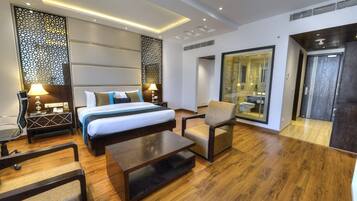 Una habitación de hotel moderna con una cama grande, una zona de estar y un baño con paredes de vidrio.